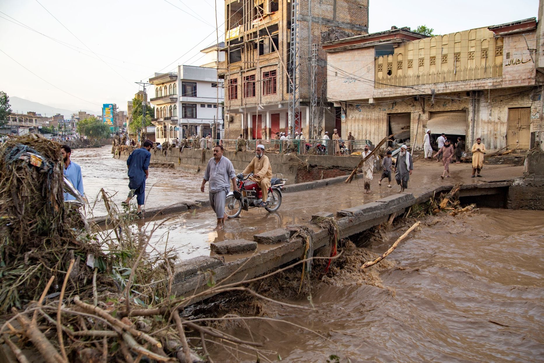 People cross a bridge in the middle of a flooded city in Pakistan.