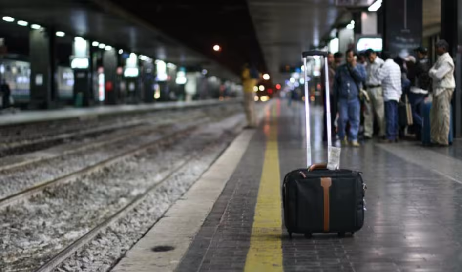 A suitcase stands alone next to a train track