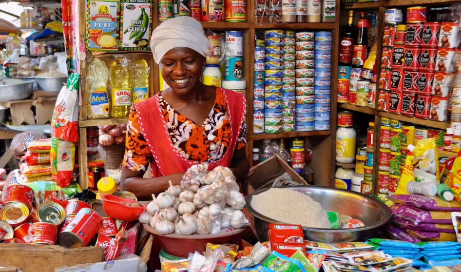 A woman at a stall smiles behind a counter full of goods for sale.