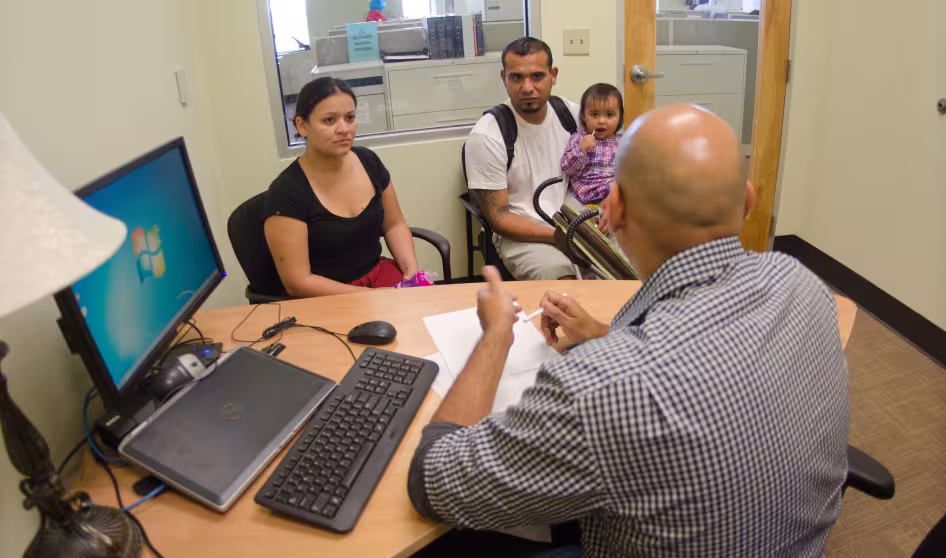 A couple and a young child talk to a man behind a desk