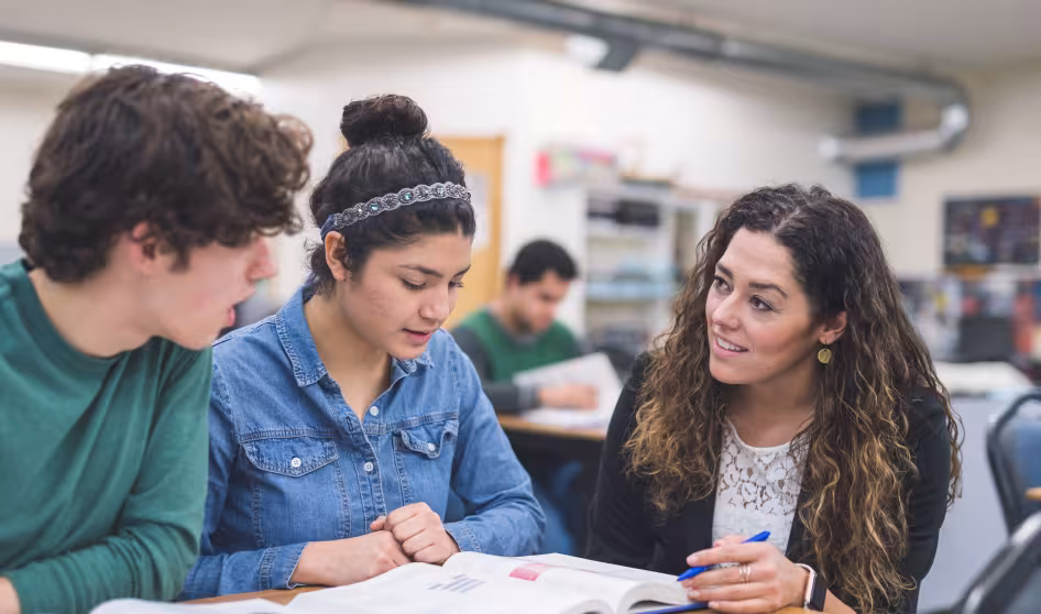 A teacher helps two high school students at their desks