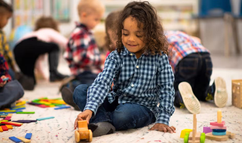 Young child seated on floor in classroom playing with a toy
