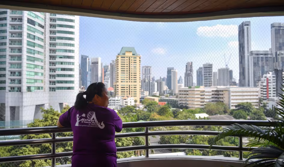 A woman in a purple shirt looks out over the skyline of Bangkok.