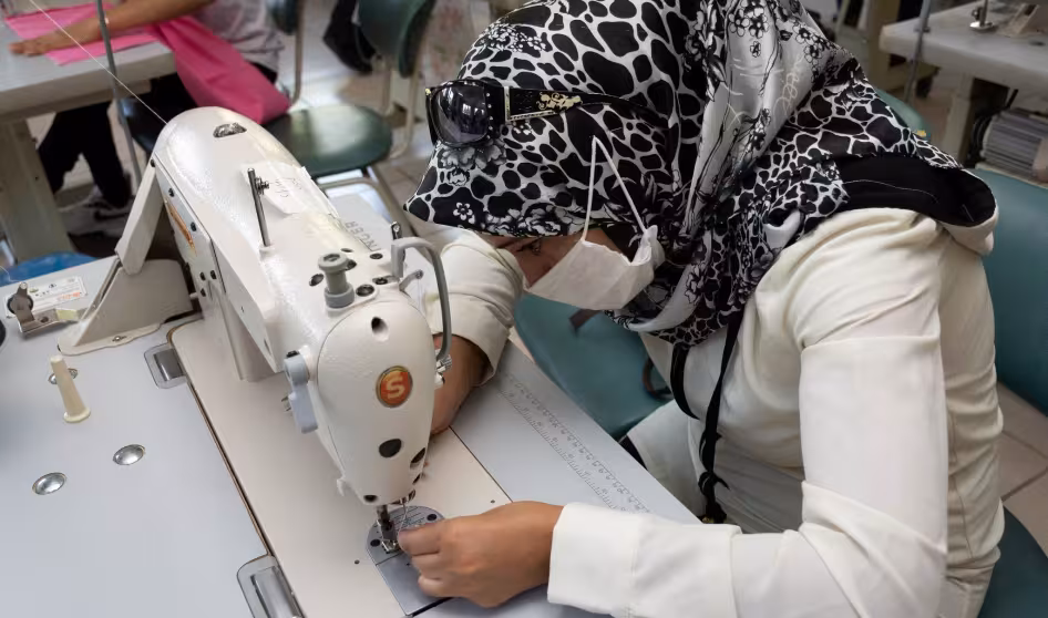 A woman in a headscarf leaning over a sewing machine.