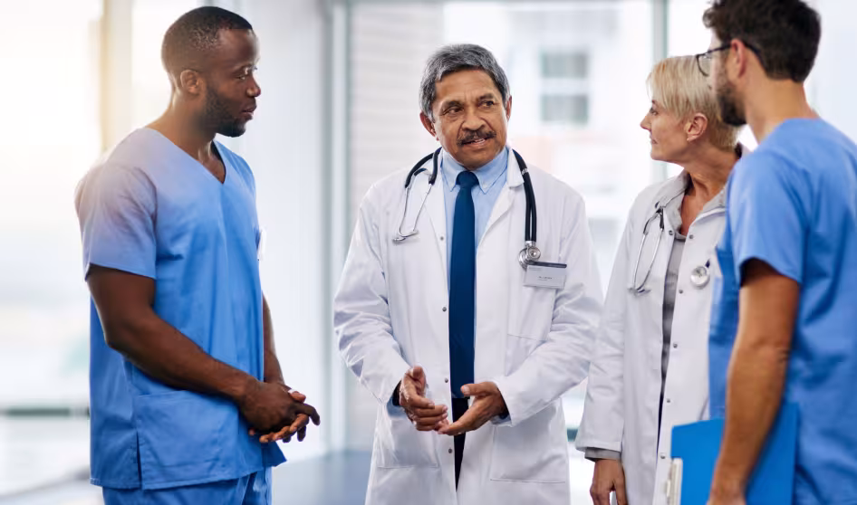 An older physician in a white coat talking to colleagues
