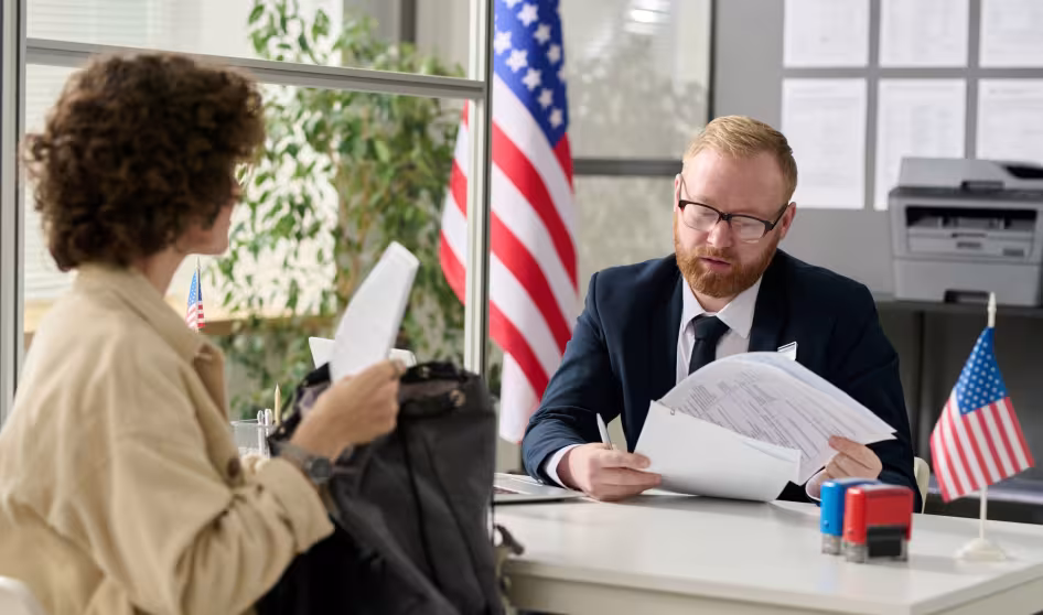 A man in a suit reviews a woman's paperwork, while the U.S. flag stands behind him