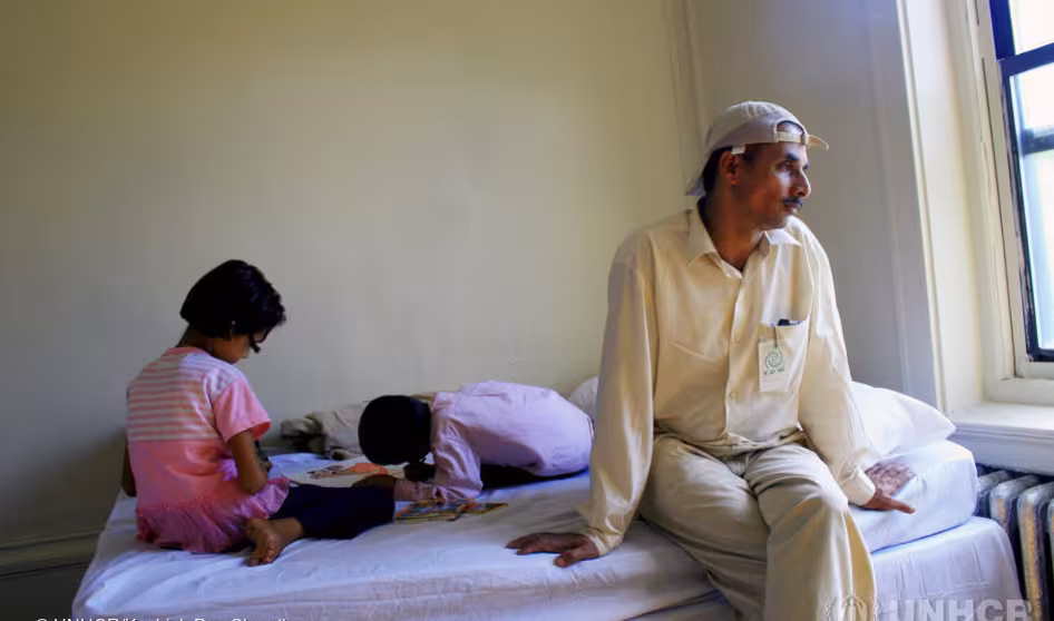 Bhutanese refugee sits on bed in family's apartment in New York