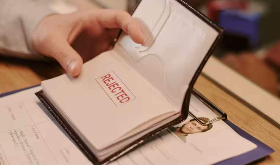 Image of a hand holding a passport with the stamp 'rejected' on a passport page
