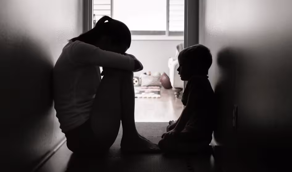 A sad mother and child sit in a dark hallway.