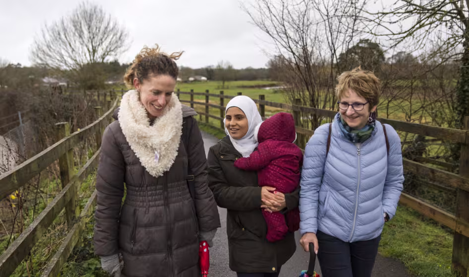 Three women, one in a headscarf and holding a baby, walk in the countryside in Devon, UK