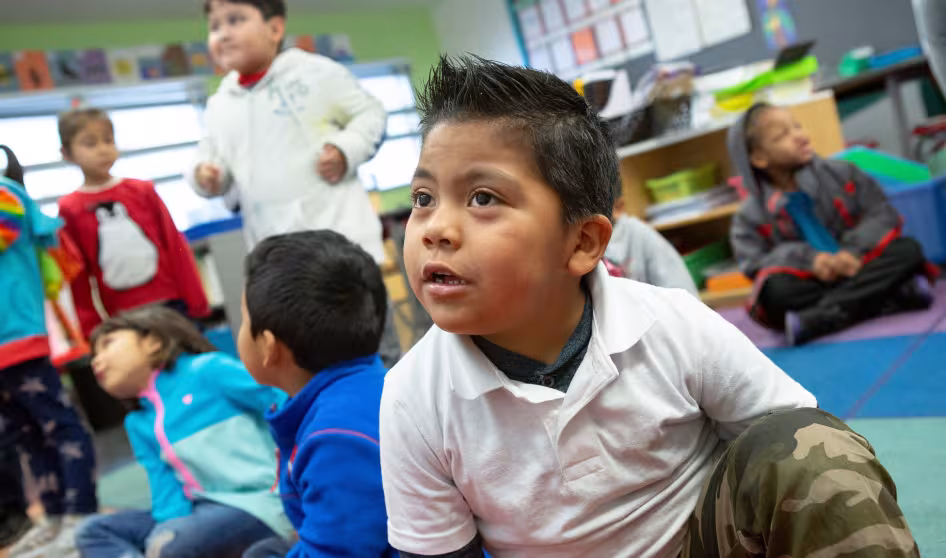 A prekindergarten student sitting on the floor with classmates