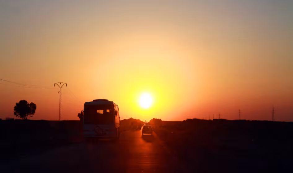 Vehicles drive down a road near the Tunisia-Libya border with the sun in the background