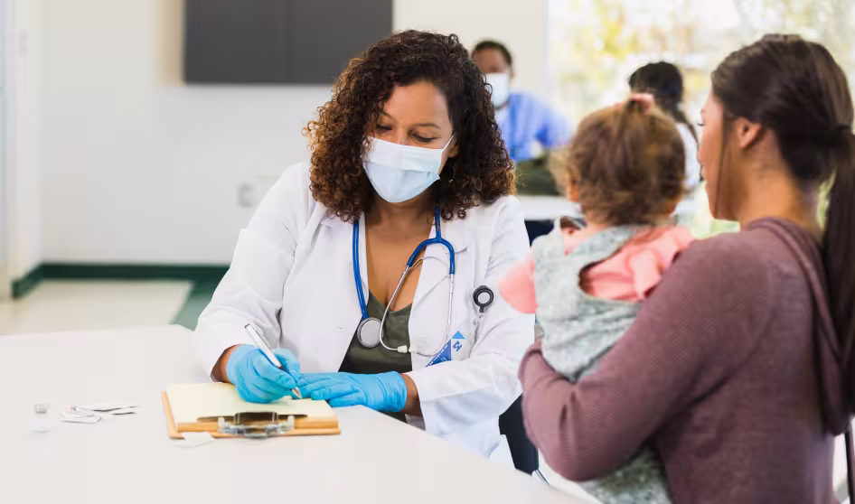 A woman holding a young child talks to a female pediatrician at a free clinic