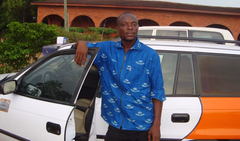 A man stands next to a taxi he got with the help of IOM's AVRR program