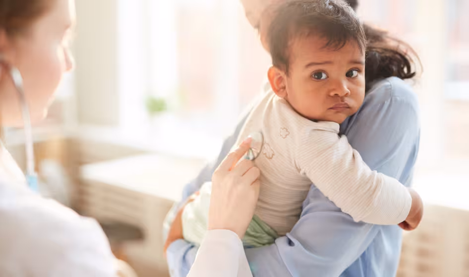 Mother holds her young child while doctor examines him with a stethoscope