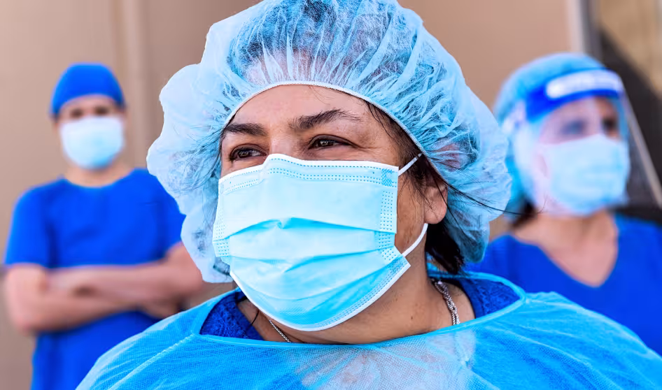 Three health-care workers wearing blue protective masks and gowns
