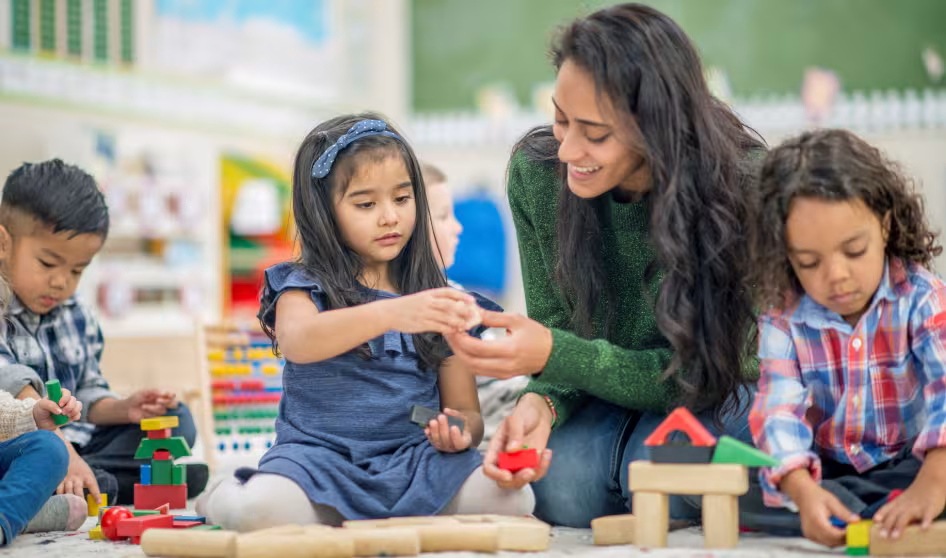 A teacher and group of young children play with blocks
