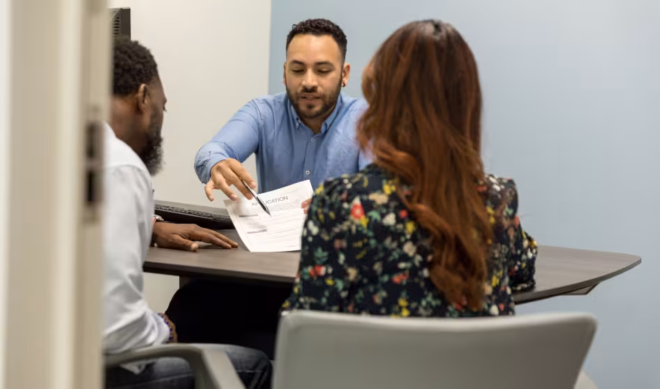 Three people sit at a desk and discuss a form