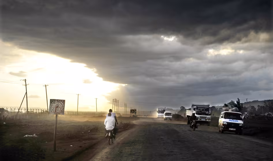Motorbikes and cars travel down a road in a storm