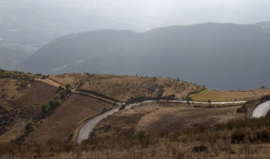 A road cuts across mountains and hills, with clouds in the background, in Huehuetenango, Guatemala