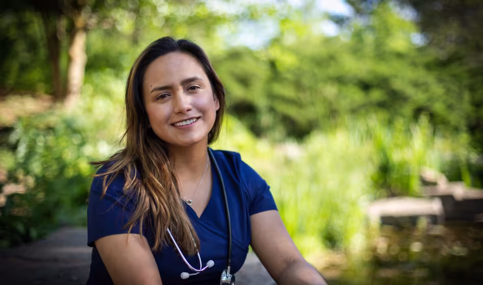 A young female nurse wearing medical scrubs and a stethoscope sits on a park bench