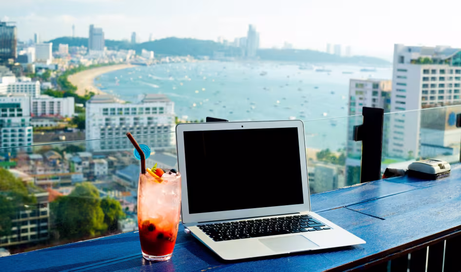 A laptop and cocktail on a ledge overlooking the beach