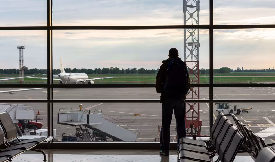 A man with a backpack stands in an airport and looks at a plane