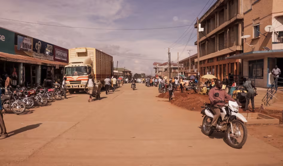 Motorcyclists and pedestrians travel a road between buildings in Arua, Uganda