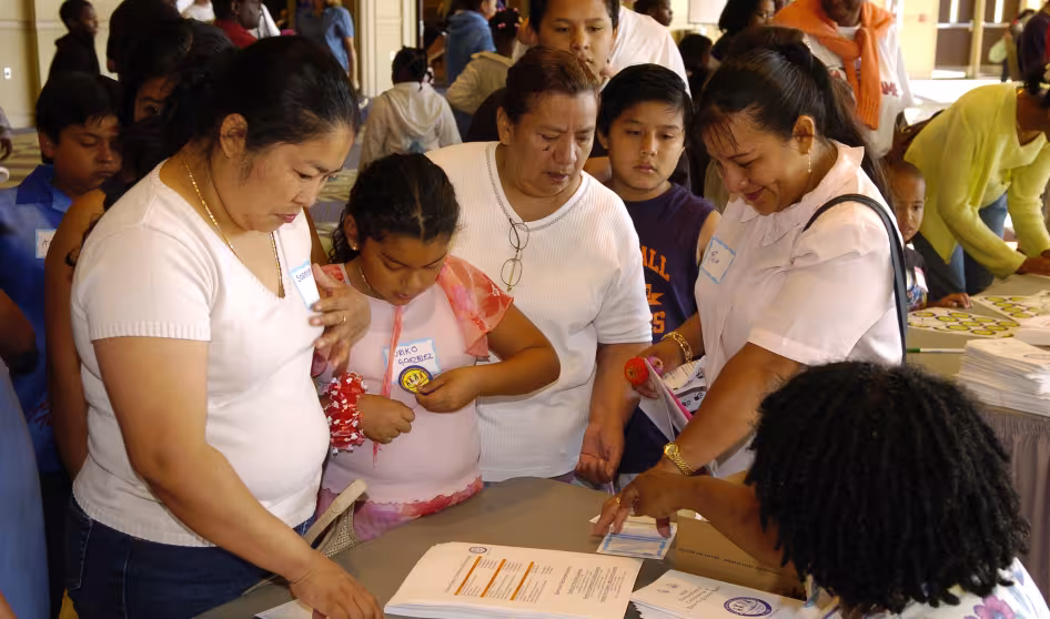 Parents and their children talk to another adult seated at a table at a Parents & Family Conference
