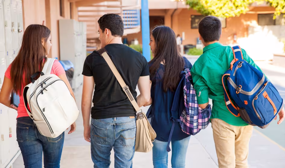 Four high school students with backpacks walk together at a school
