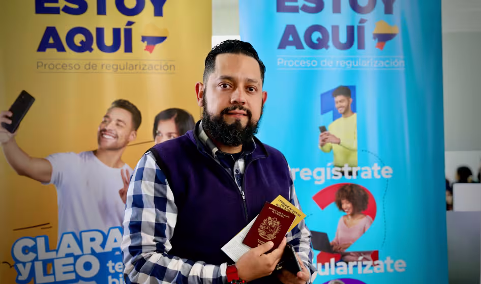A Venezuelan man holds a passport in front of a sign for Ecuador's regularization process