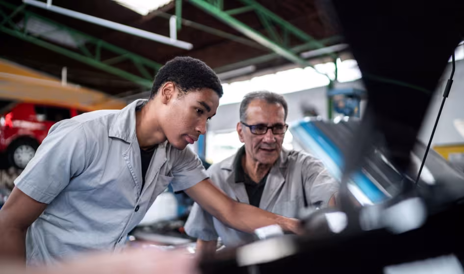 Auto mechanics, one young and one old, look at a car engine in a repair shop