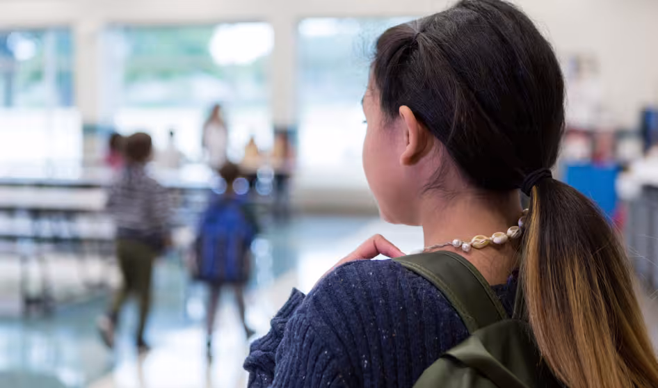 A middle school girl standing alone in a school cafeteria