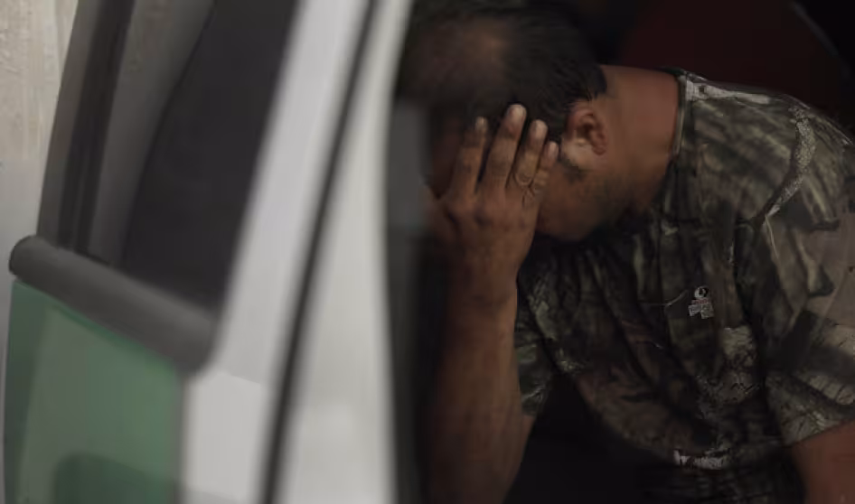 An apprehended migrant sits in a truck with his hands in his face