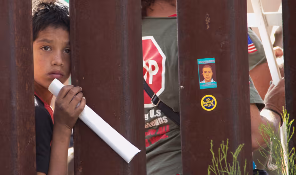 A boy peers through fencing at the U.S.-Mexico border. 