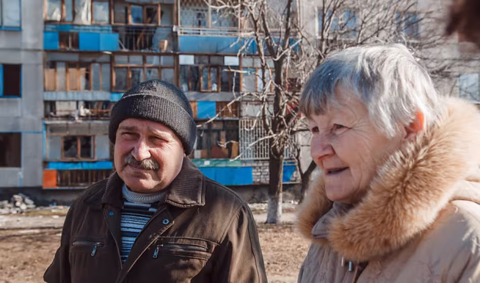 An older man and woman stand in front of an apartment building
