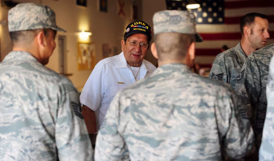 Two men in military attire stand with a veteran