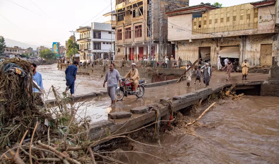 People cross a bridge in the middle of a flooded city in Pakistan.