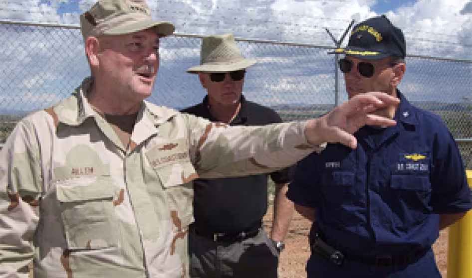 Officials from the Coast Guard and Border Patrol meet along a stretch of SBI fence in Arizona.