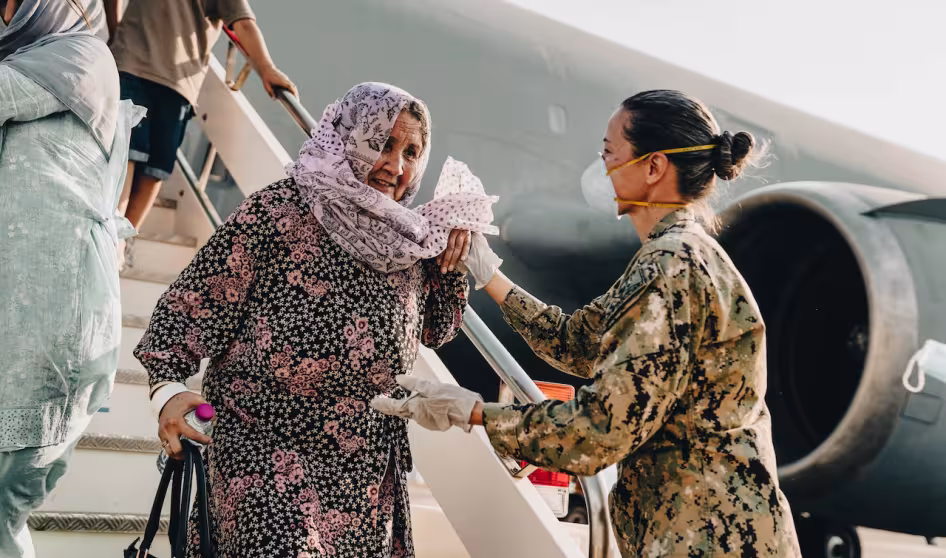 A U.S. service member helps an older Afghan woman off a plane at a naval air station