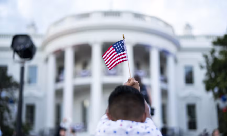 A child holds up a U.S. flag in front of the White House.
