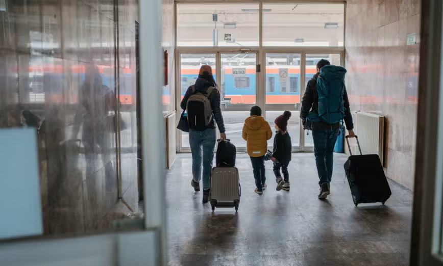 The backs of two adults and two children pulling luggage in a train station
