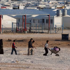 Children roll a wheelbarrow through a refugee camp