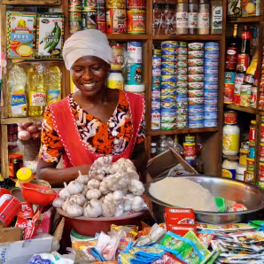 A woman at a stall smiles behind a counter full of goods for sale.