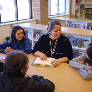  A high school teacher and students sit around a table in a school library