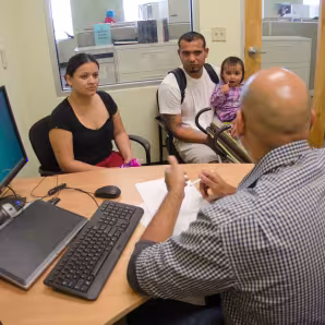 A couple and a young child talk to a man behind a desk