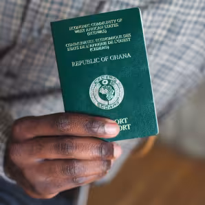 A green passport from Ghana held in a person's hand.
