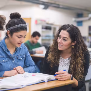 A teacher helps two high school students at their desks