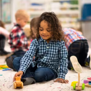 Young child seated on floor in classroom playing with a toy