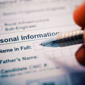 A pen poised above a form reading "Personal Information: Name in Full"